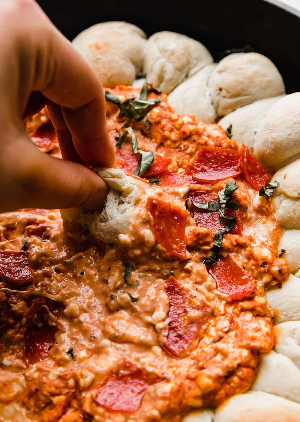 A pizza roll being dipped into a cream cheese pizza dip.