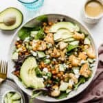 Roasted Cauliflower Salad in a large white bowl topped with sliced avocado and honey mustard dressing.