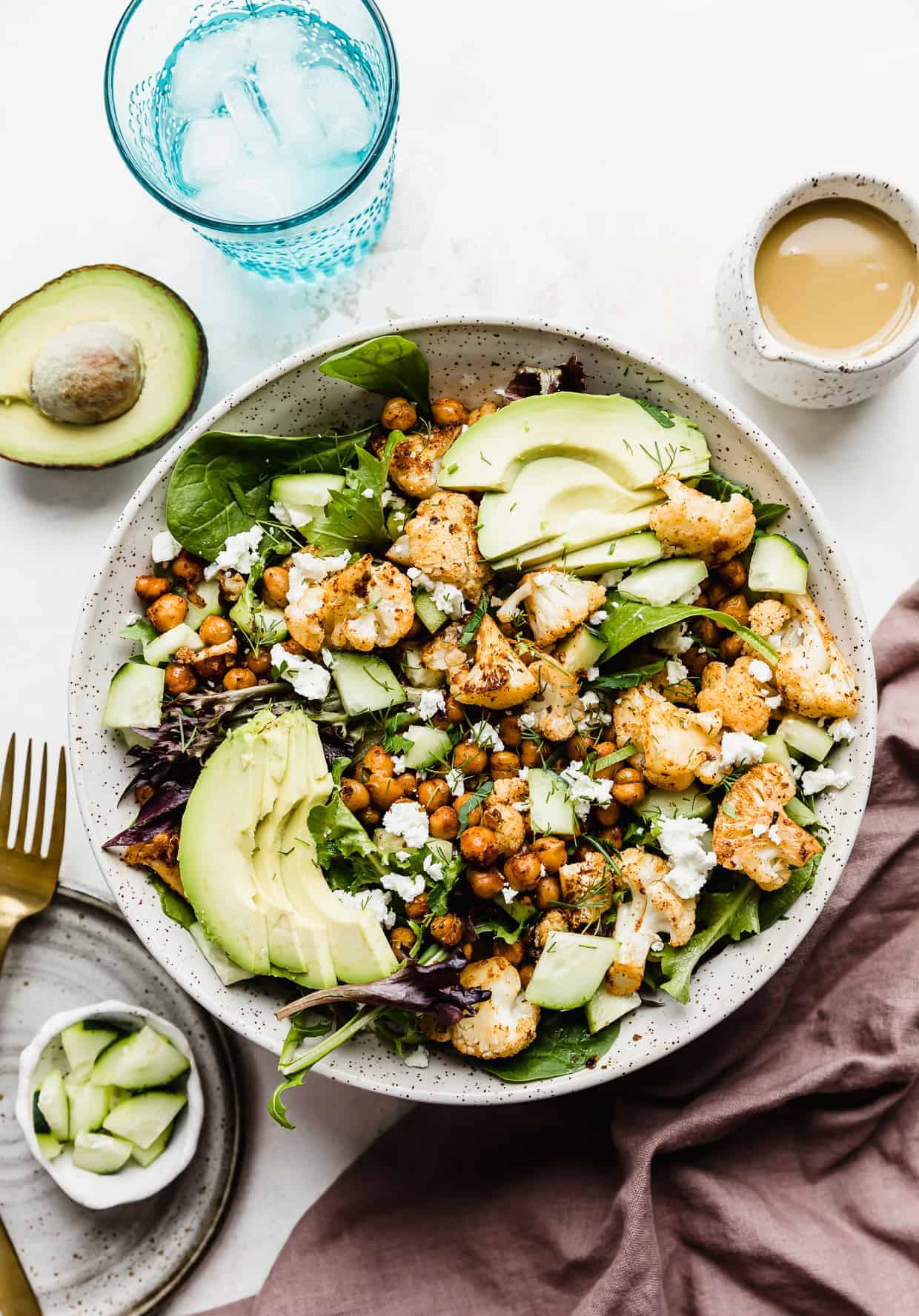 Roasted Cauliflower Salad in a large white bowl topped with sliced avocado and honey mustard dressing.
