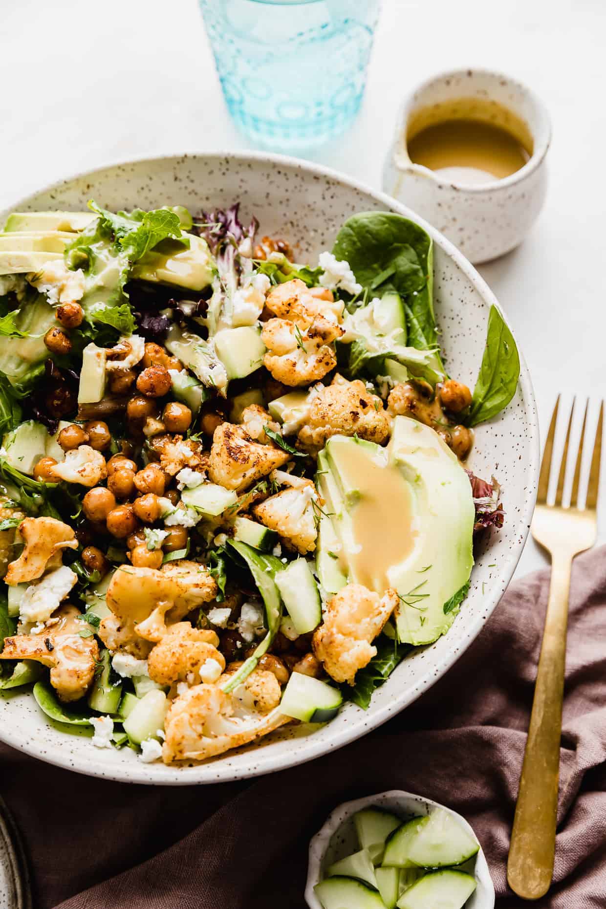 A salad in bowl topped with roasted cauliflower, sliced avocado, roasted chickpeas and a creamy yellow dressing.