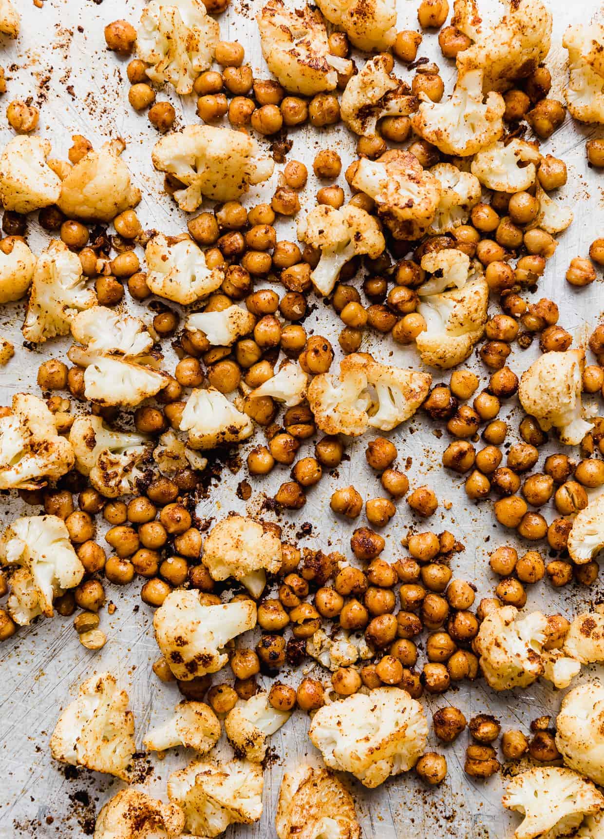 Roasted cauliflower florets and chickpeas on a silver baking sheet.