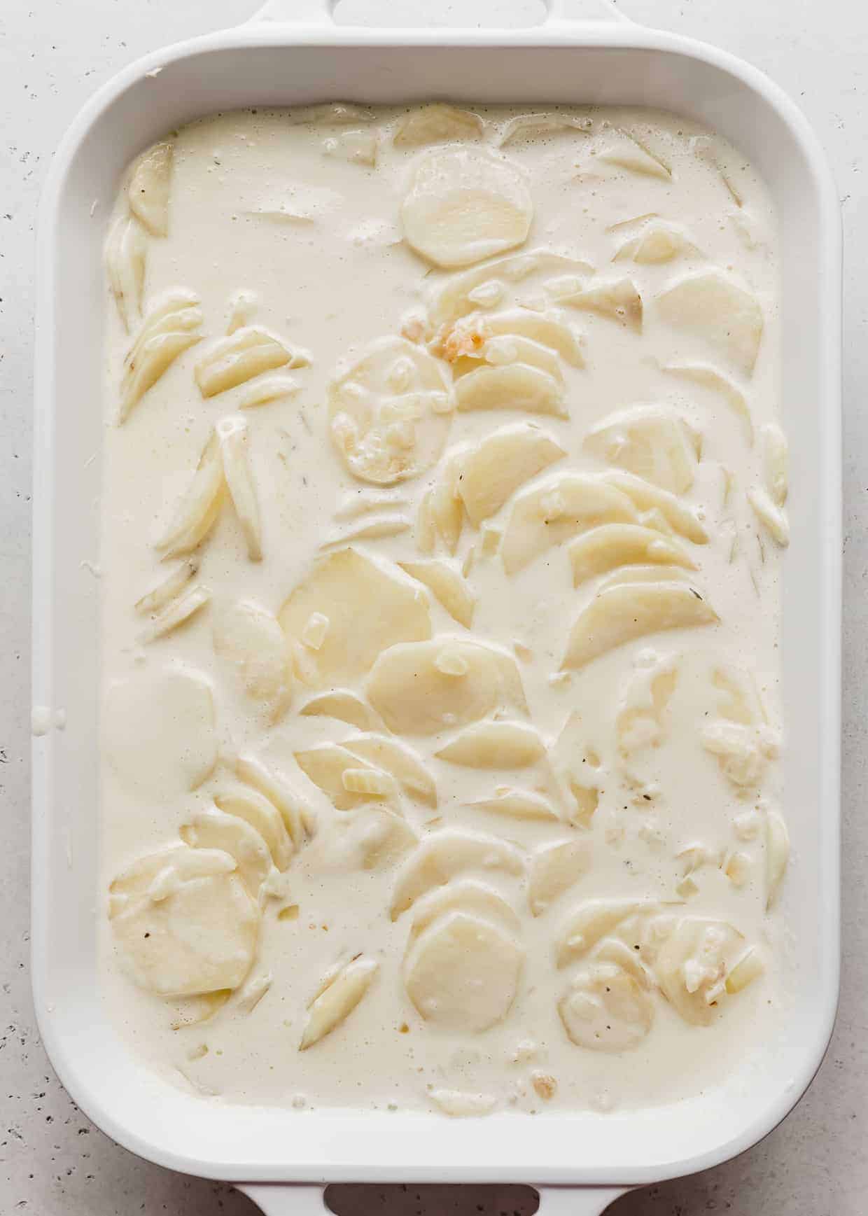 A white casserole dish full of thinly sliced potatoes loaded with heavy cream.