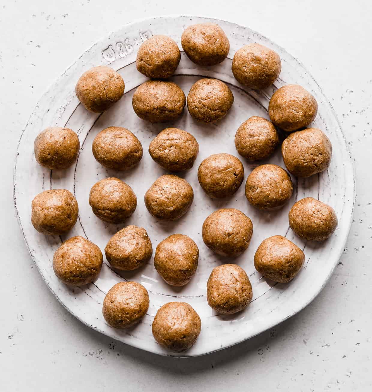 A white plate full of brown Snickerdoodle Energy Bites against a light gray background.