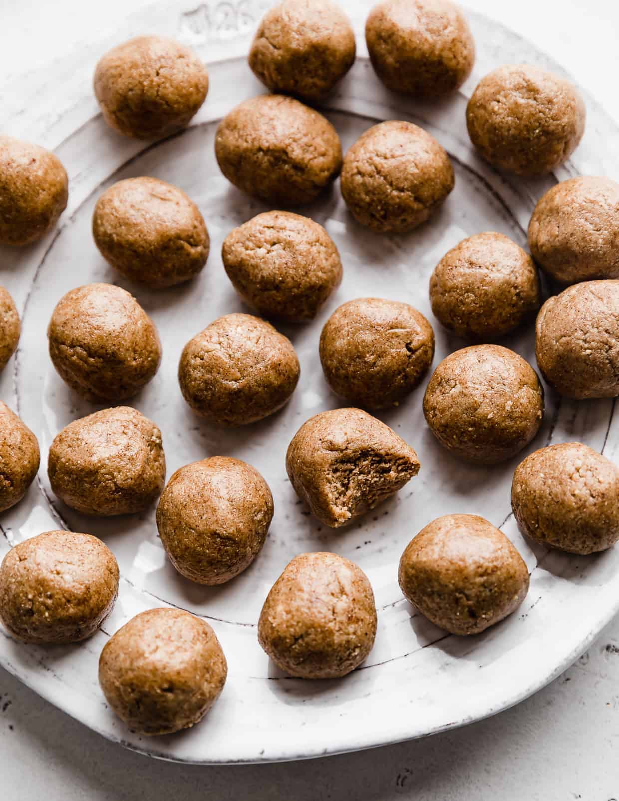 A white plate full of Snickerdoodle Energy Bites, with a bite taken out of the middle energy ball. 