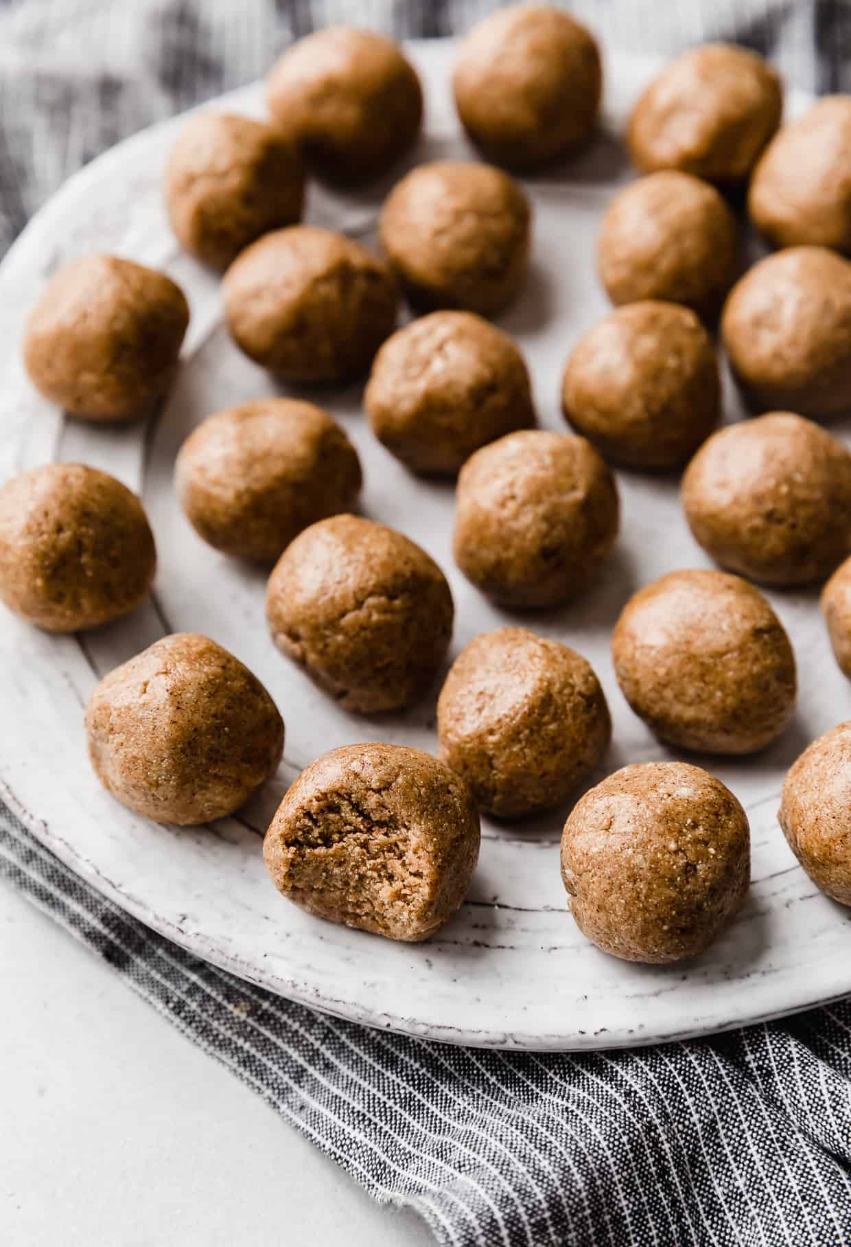 Snickerdoodle Energy Bites rolled into balls, sitting on a white plate with the closest one with a bite taken out of it.