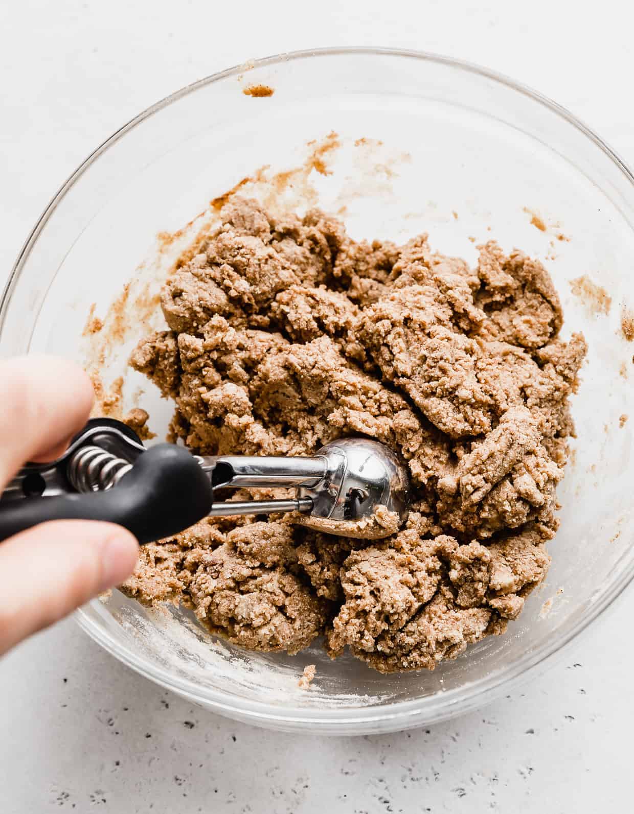 A small cookie scoop dipping into Snickerdoodle Energy Bites batter. 