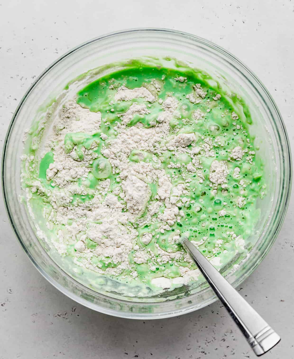 A glass bowl with green pancake batter in it.