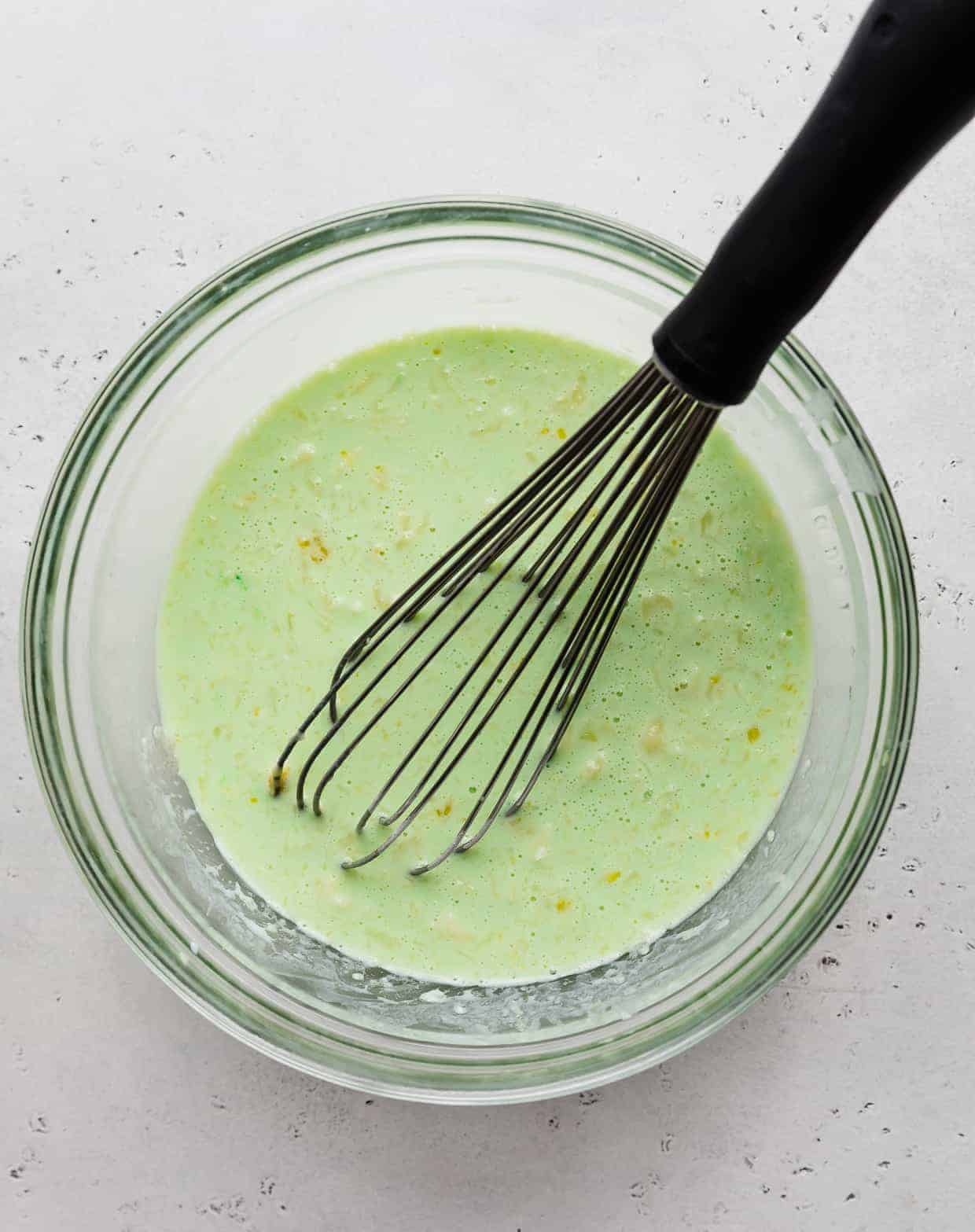 A green mixture in a glass bowl with a whisk in it. 