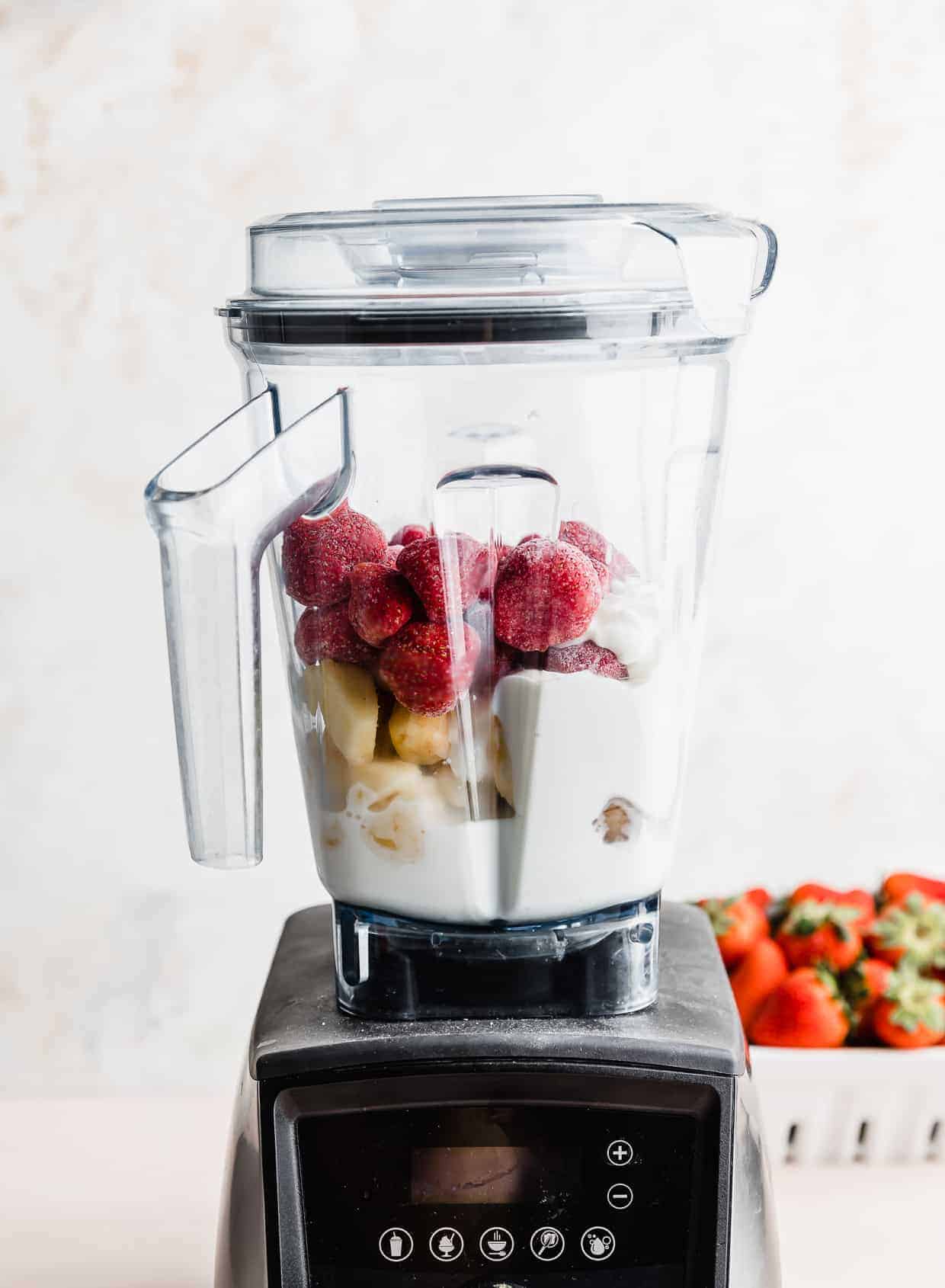 A Vitamix blender full of ingredients used to make a pineapple and strawberry smoothie against a white background.