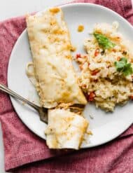 A white plate with 1 sweet lime Chile enchilada on it, with a fork cutting a portion of the enchilada.