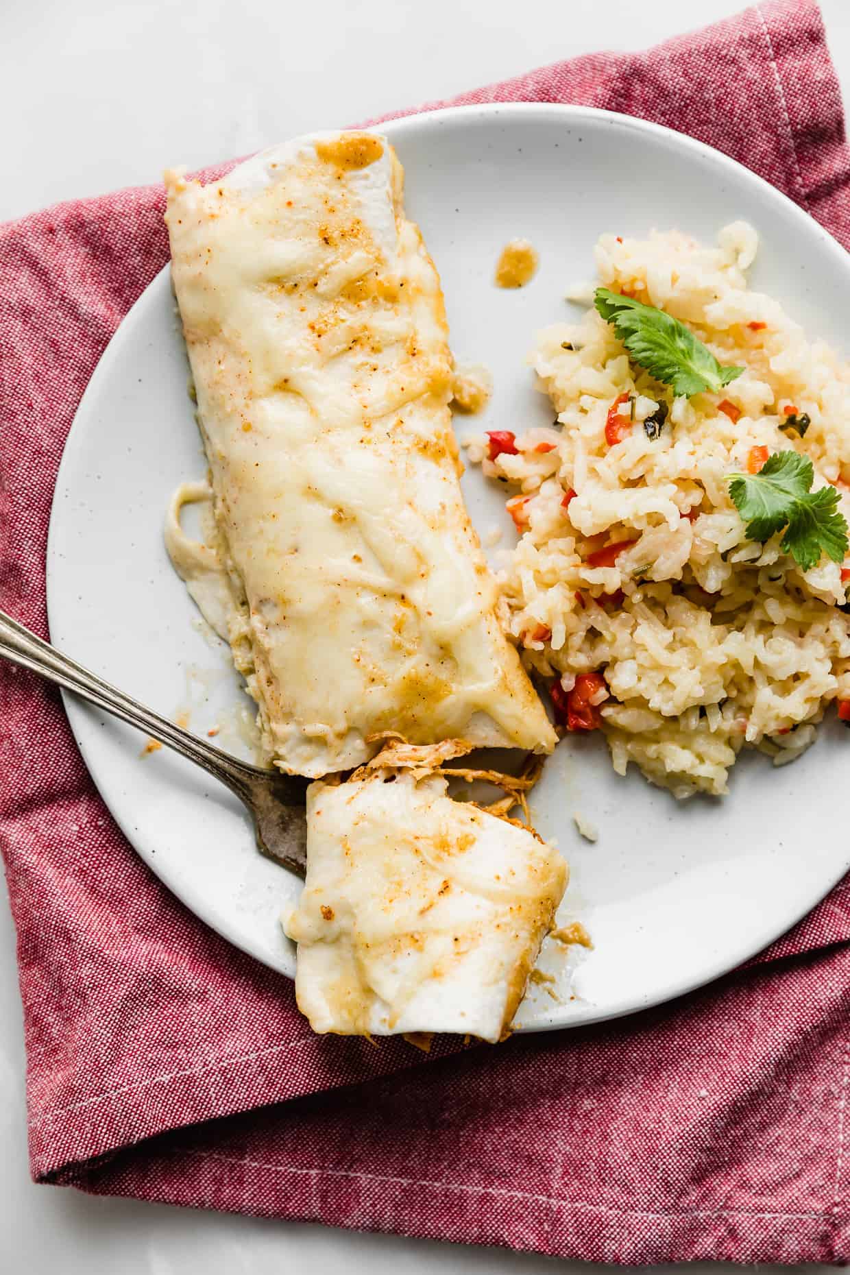 A white plate with 1 sweet lime Chile enchilada on it, with a fork cutting a portion of the enchilada. 
