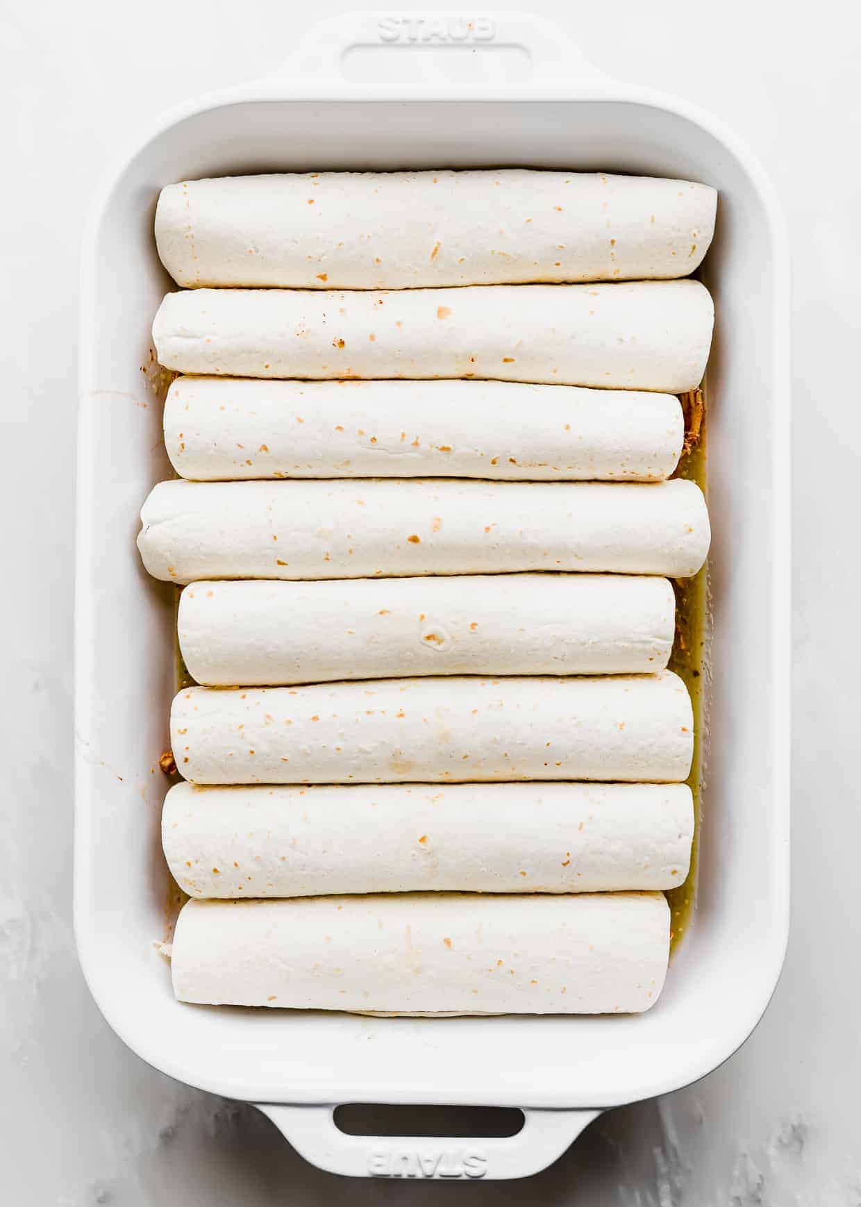 Eight rolled up enchiladas in a white casserole dish.