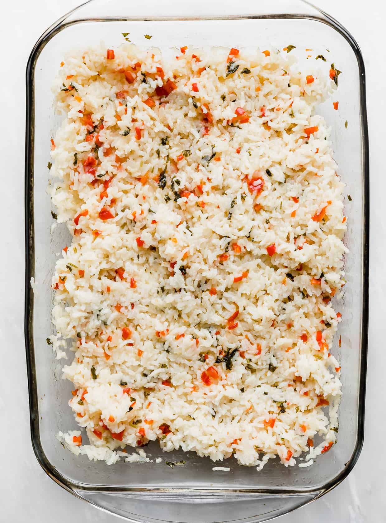 A glass baking dish full of Sweet Pepper Rice with red and green studded peppers and cilantro throughout. 