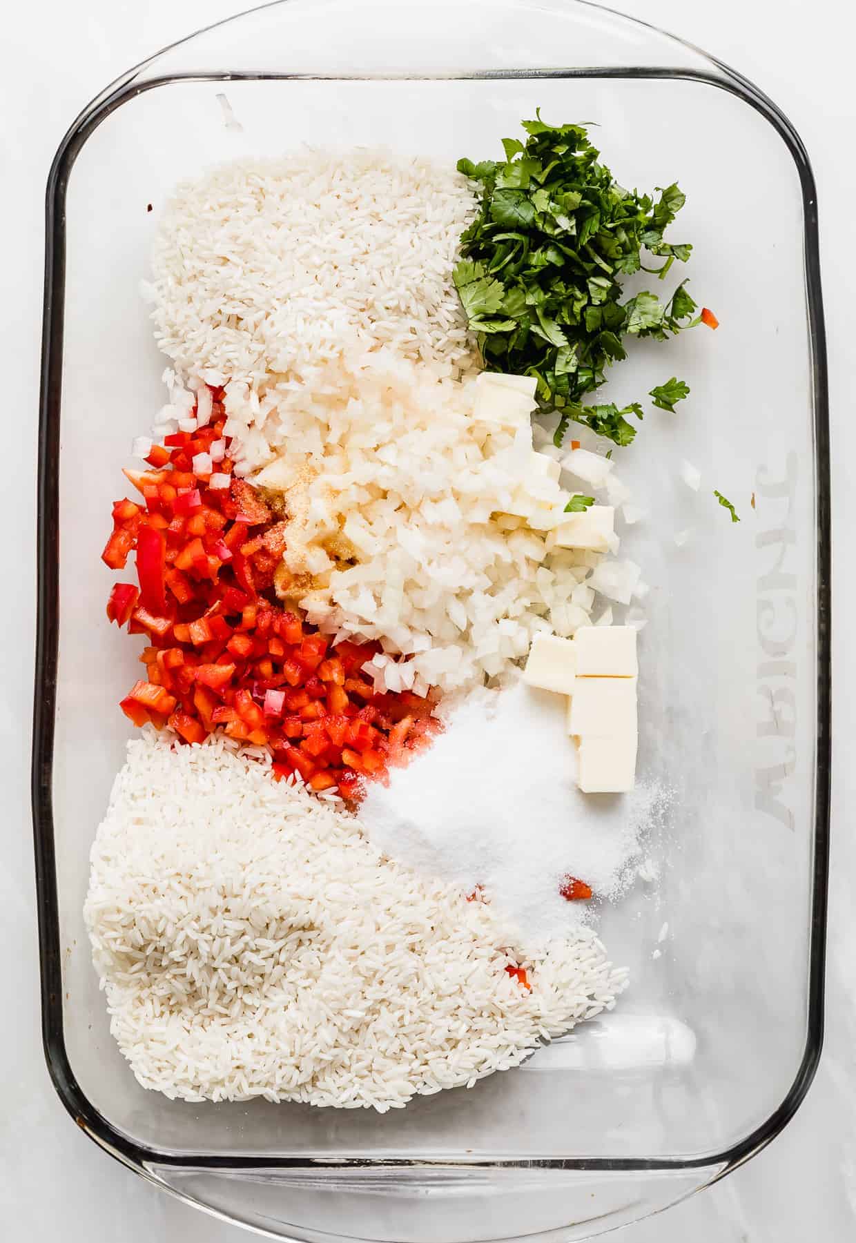 A glass baking dish with chopped red pepper, cilantro, white rice, sugar, salt and spices in it.