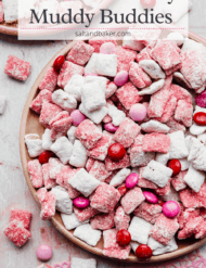 White and pink covered Chex mix on a plate with red, pink, and white M&M's dispersed throughout.