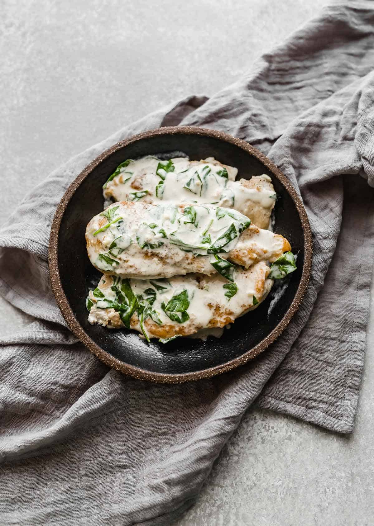 Overhead photo of Chicken Dijon breasts topped with fresh spinach on a black plate on a gray napkin.