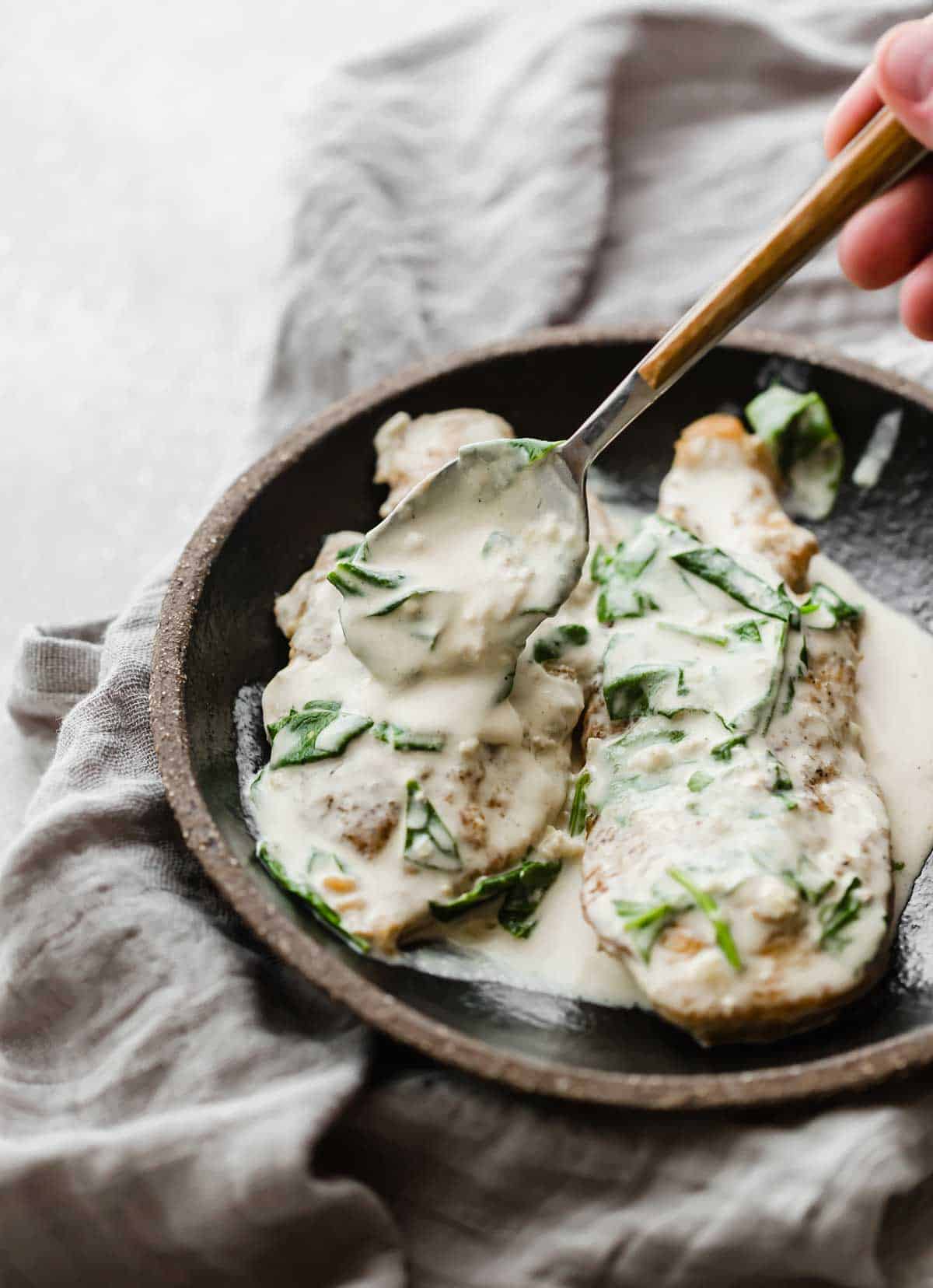 A spoon scooping a creamy spinach sauce overtop a plate of Chicken Dijon Recipe.