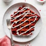 Two Red Velvet Waffles that are drizzled with a cream cheese glaze, on a white plate.