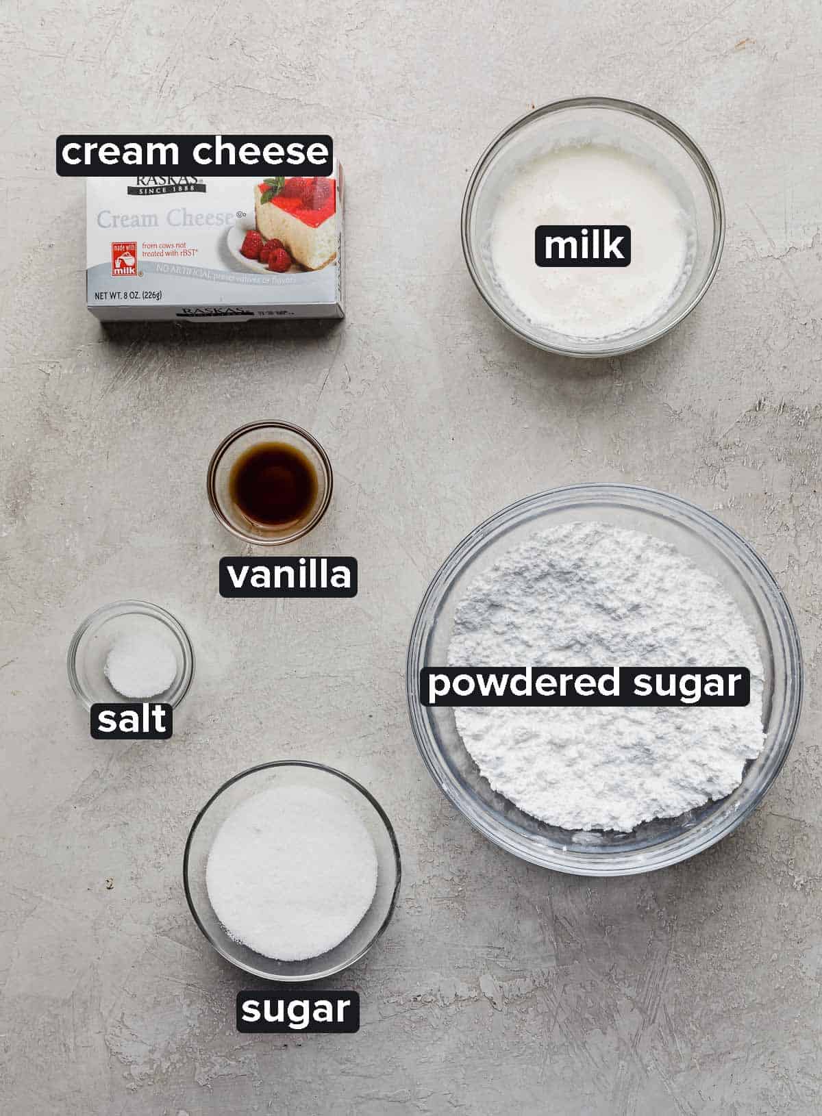 Red Velvet Waffles cream cheese glaze ingredients on a gray background: cream cheese, milk, vanilla, salt, sugar, and powdered sugar.