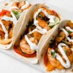 Sheet Pan Shrimp Fajitas drizzled with white Lime Crema on a white plate and white background.