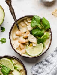 A bowl of The Best White Chicken Chili topped with a lime wedge, cilantro, and crushed tortilla chips.