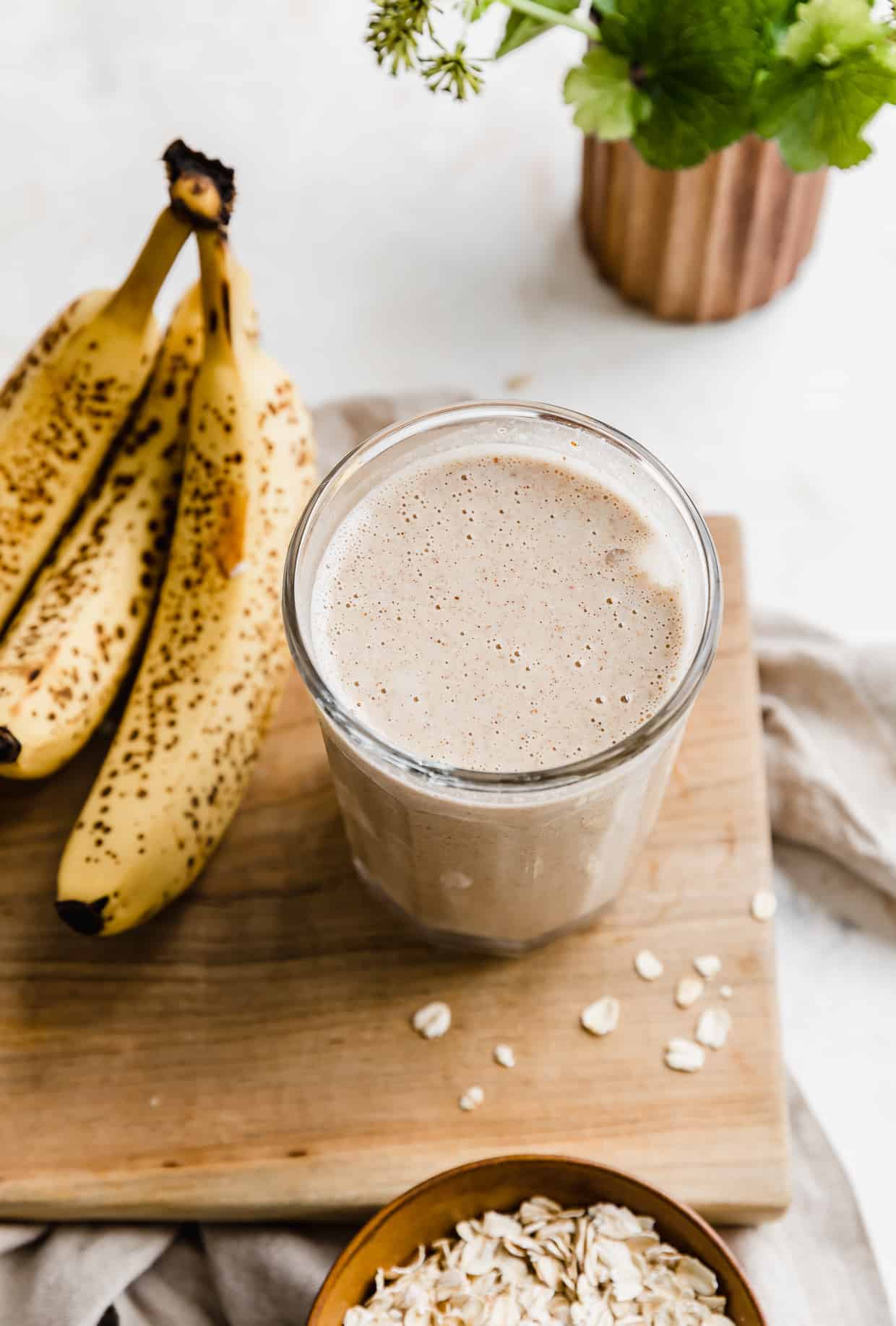 A lactation smoothie on a wooden board, with bananas next to the cup.