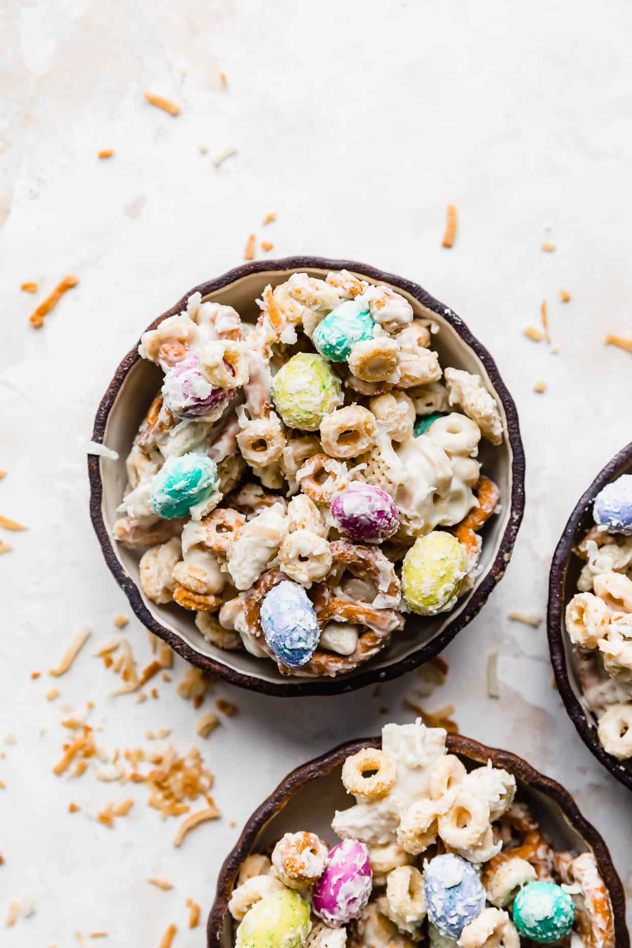 A black bowl full of Easter cereal mix against a white background that has been lightly covered in toasted coconut. 