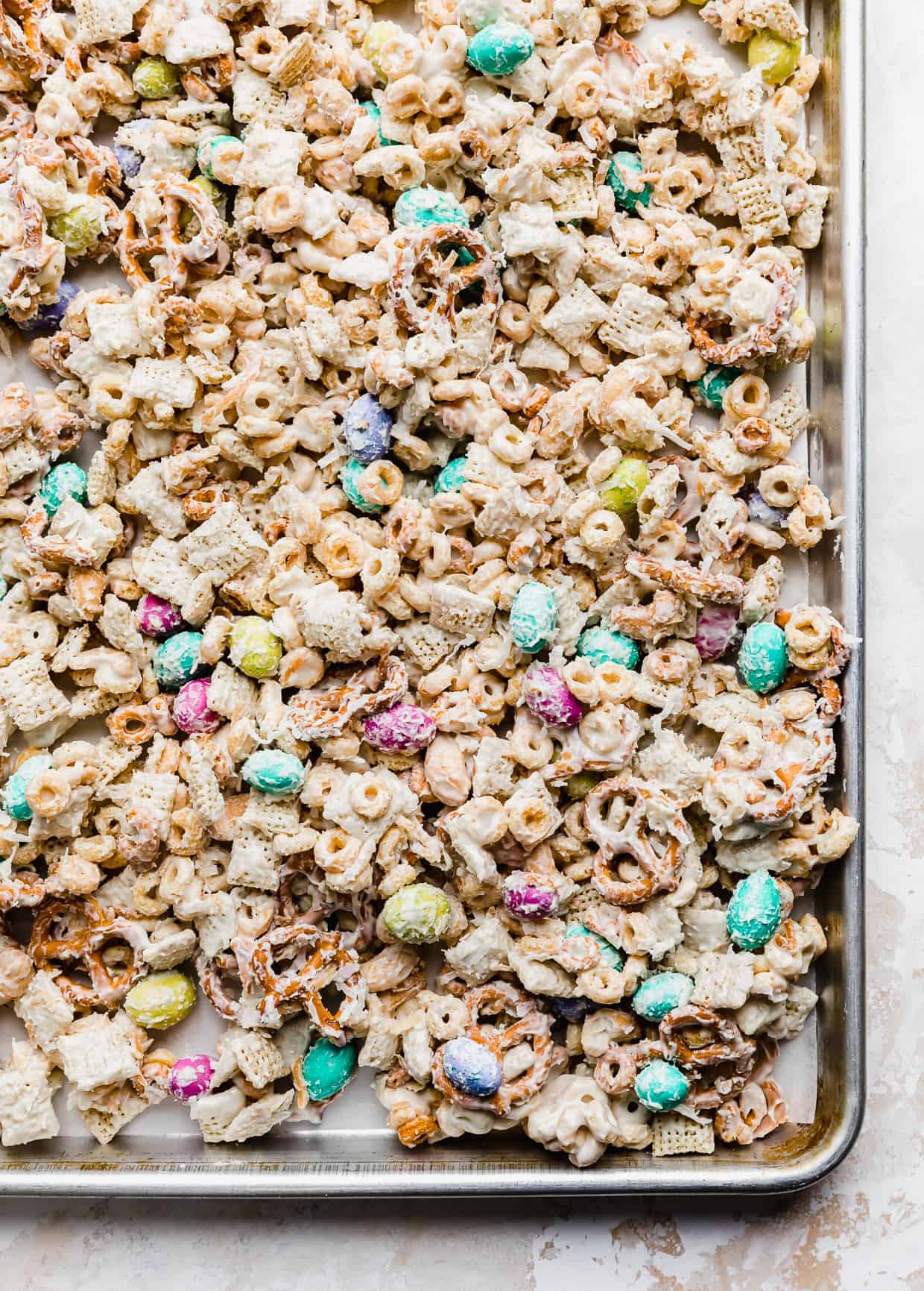 A baking sheet with white chocolate covered cereal easter trail mix dispersed on it to help it set up. 