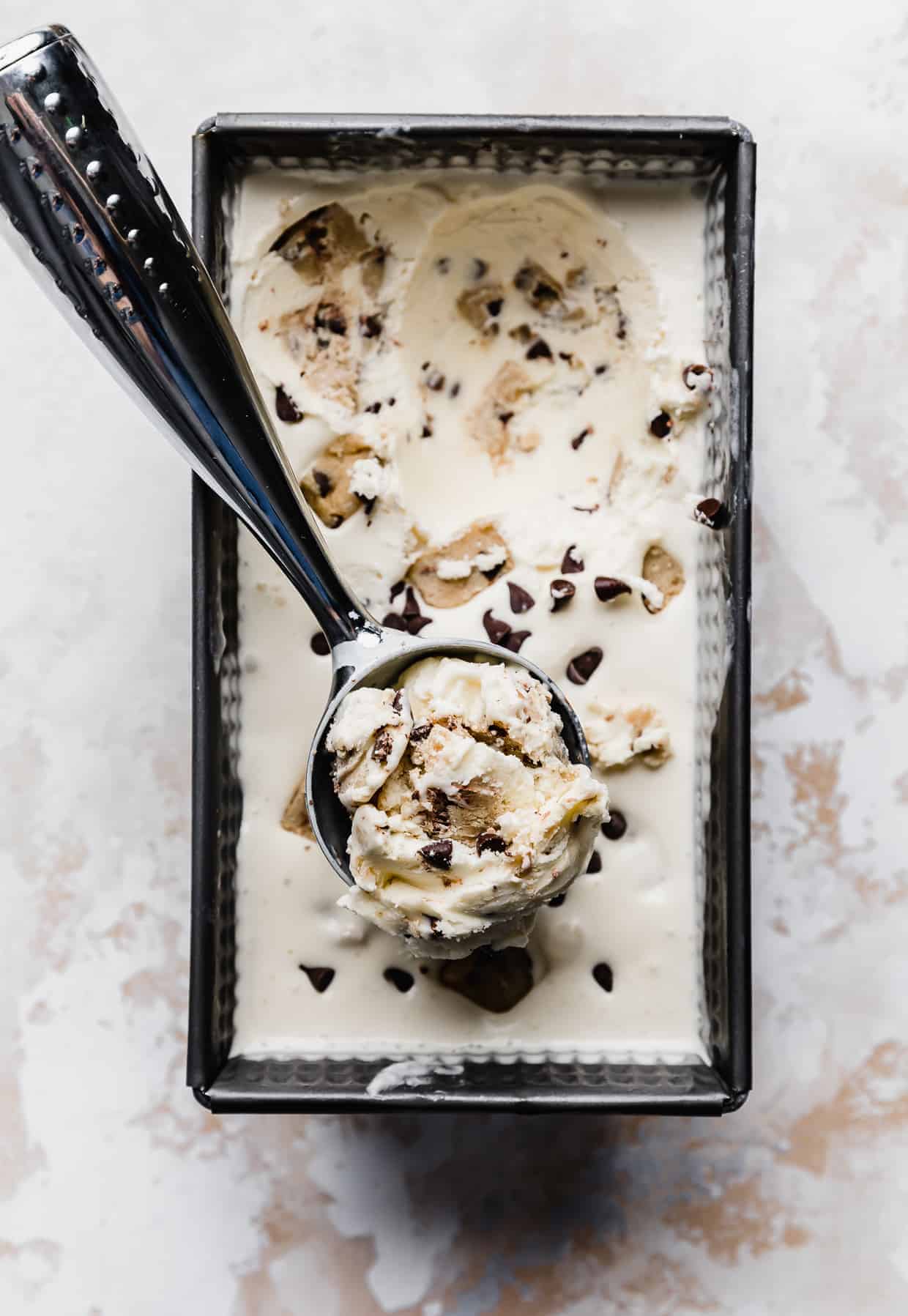 A loaf pan full of Chocolate Chip Cookie Dough Ice Cream with a cookie scoop spooning out a portion.