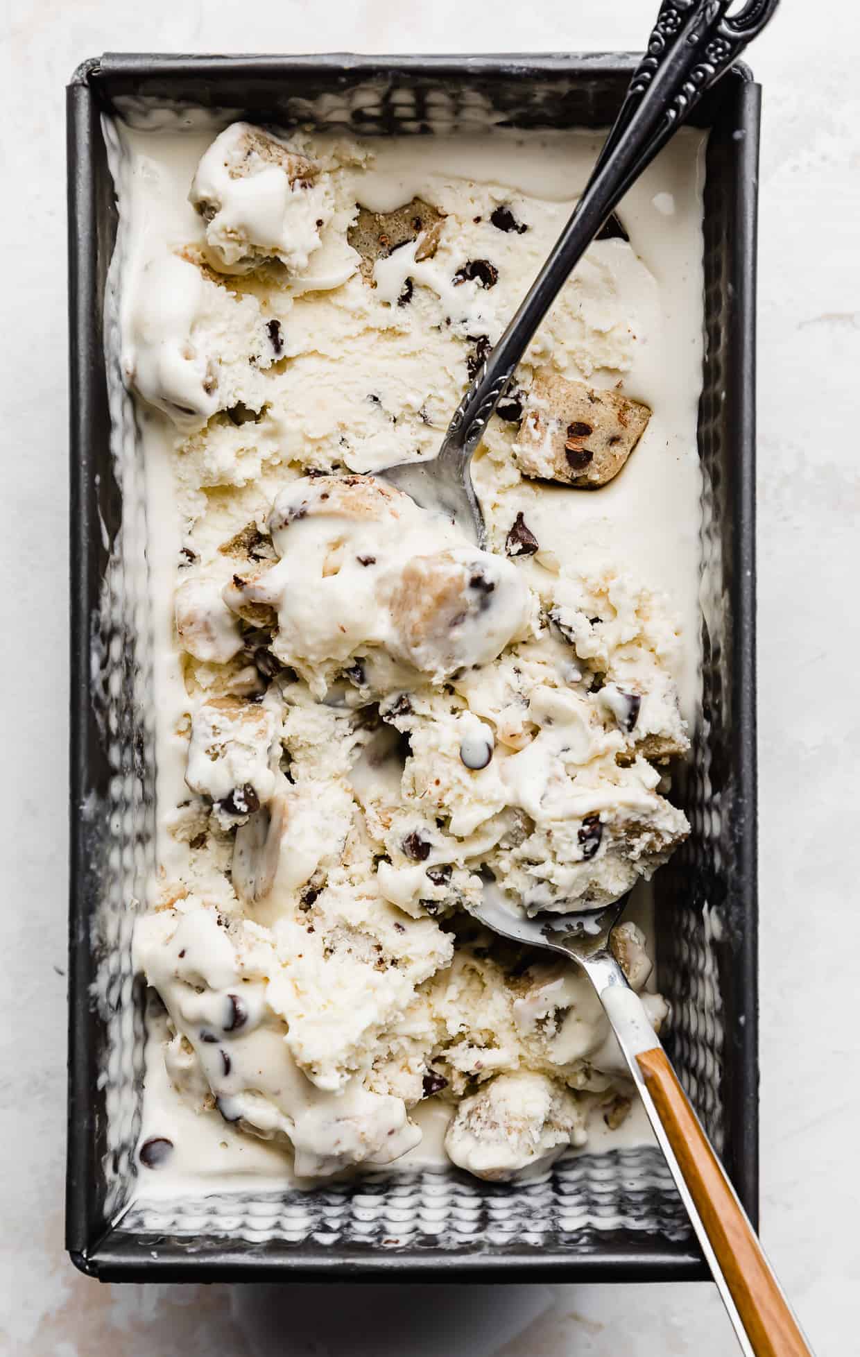 A rectangular loaf pan full of Chocolate Chip Cookie Dough Ice Cream with two spoons scooping into the ice cream.