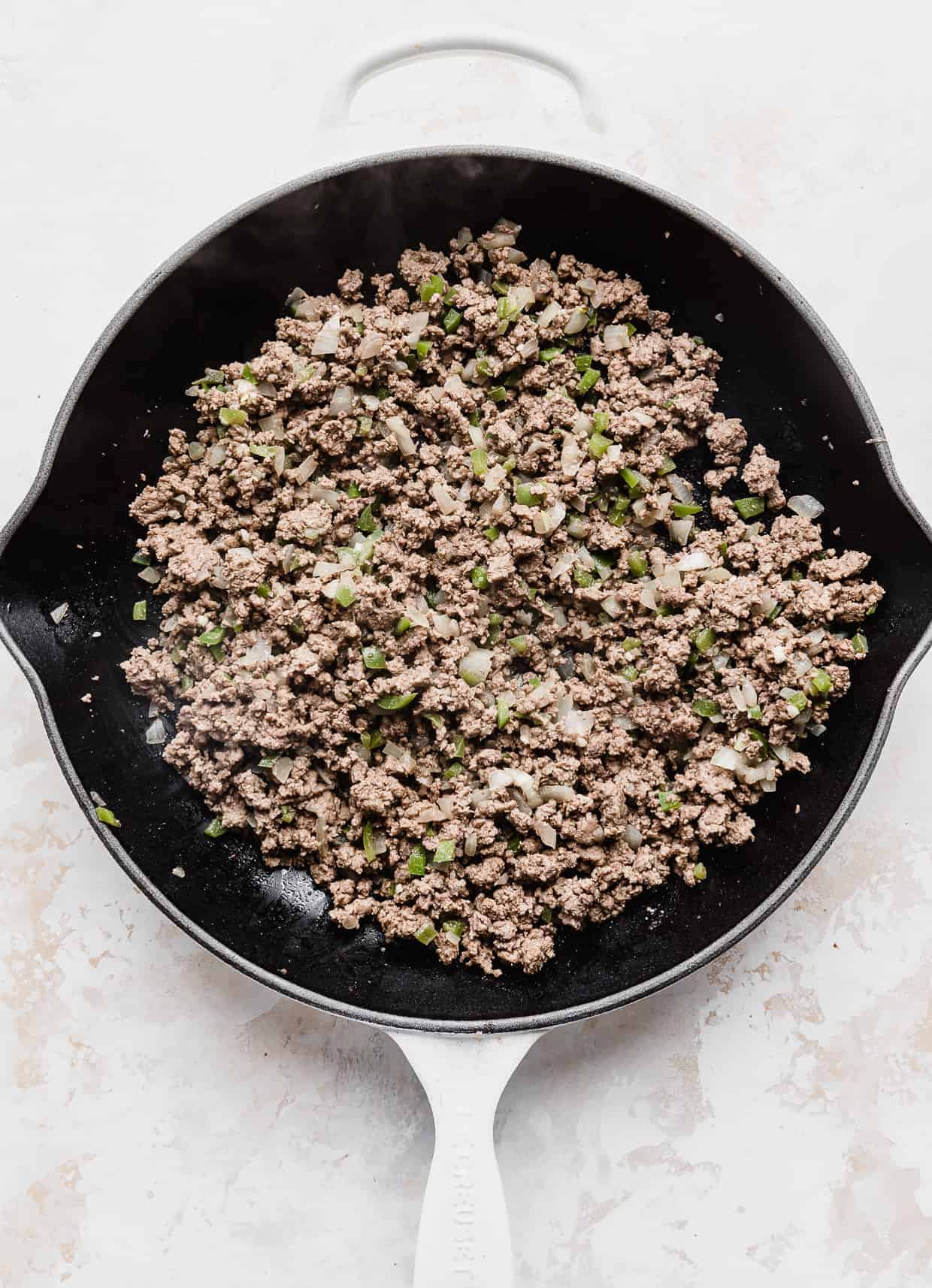 A large skillet full of cooked ground beef, diced green pepper, and onion.