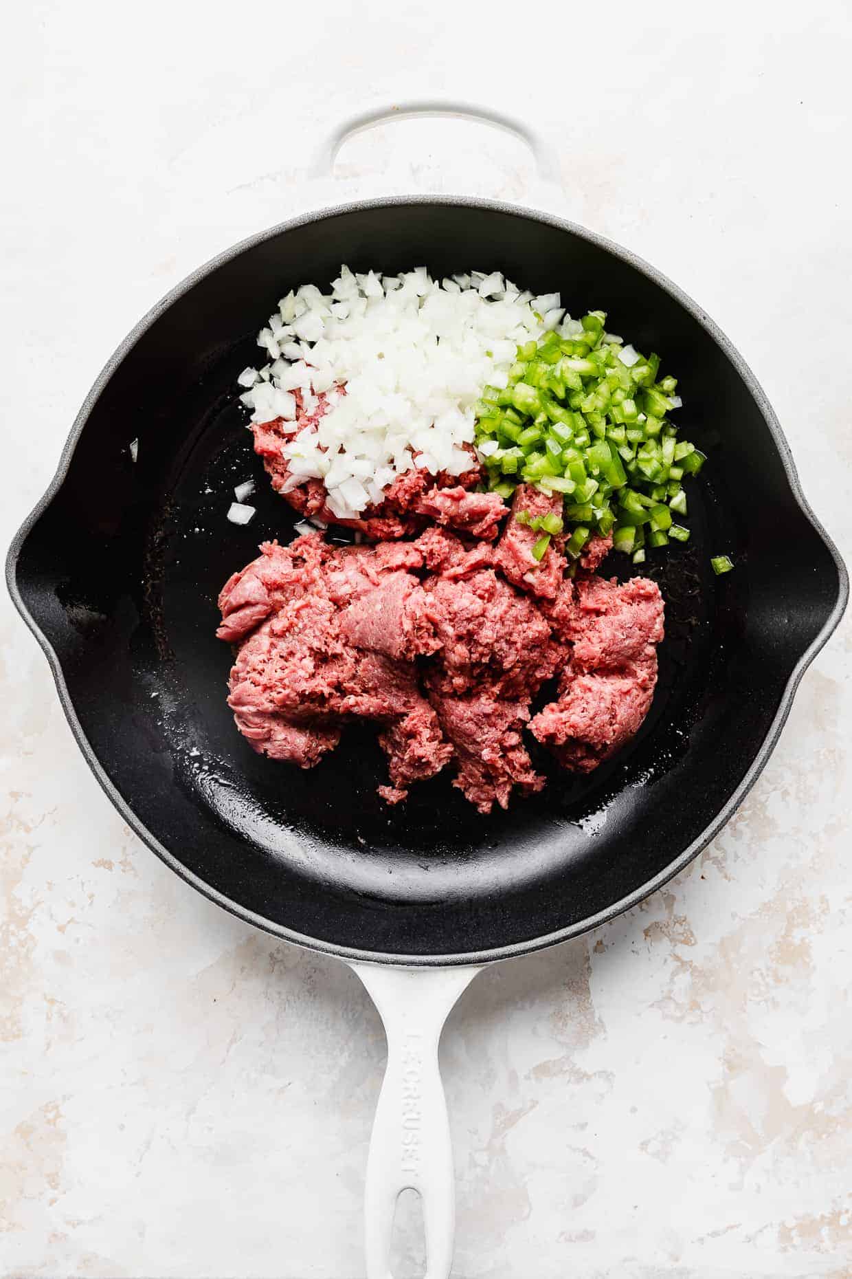 A skillet full of ingredients used to make homemade sloppy joes, against a white textured background. 