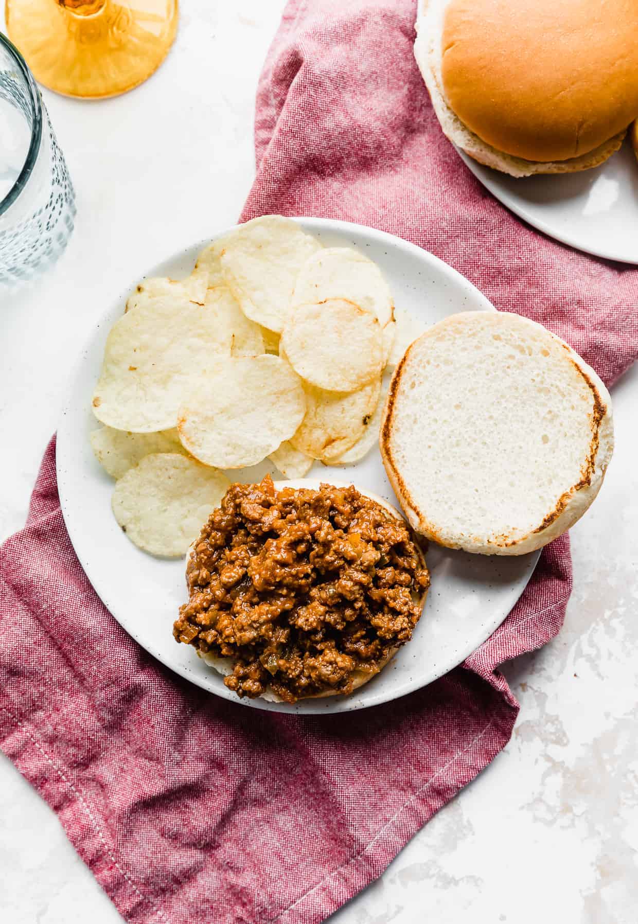 A hamburger bun on a white plate, with one half of the bun loaded with homemade sloppy Joe mix.