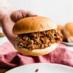 A hand holding up a hamburger bun that is very full of the best homemade sloppy Joe mix.