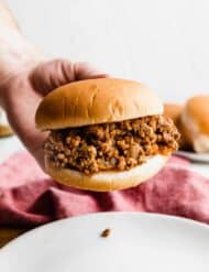 A hand holding up a hamburger bun that is very full of the best homemade sloppy Joe mix.