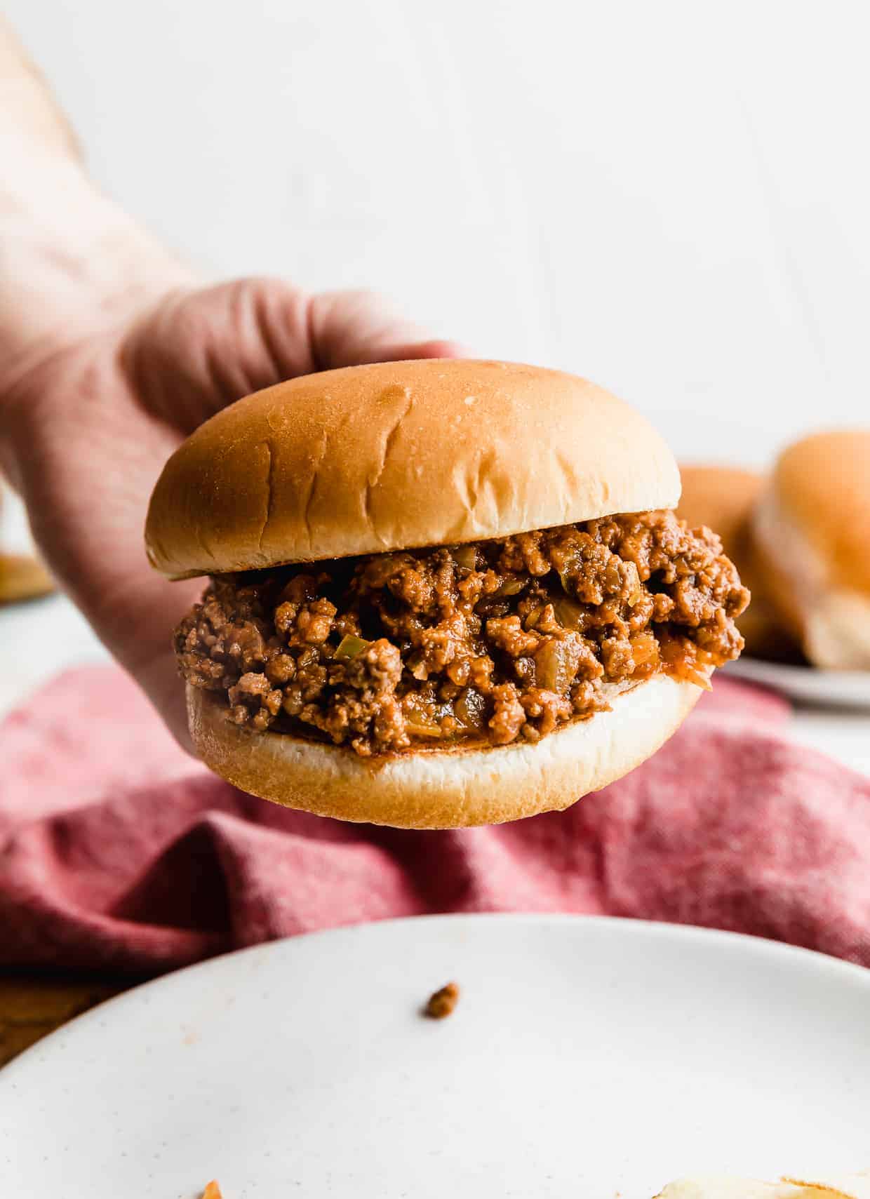 A hand holding up a hamburger bun that is very full of the best homemade sloppy Joe mix. 