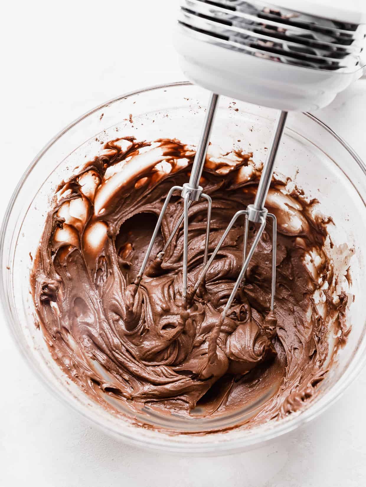 Hand beaters mixing brownie frosting in a glass bowl. 