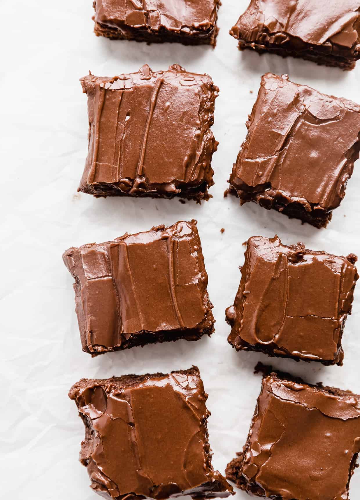 A row of frosting covered brownies on a white background.