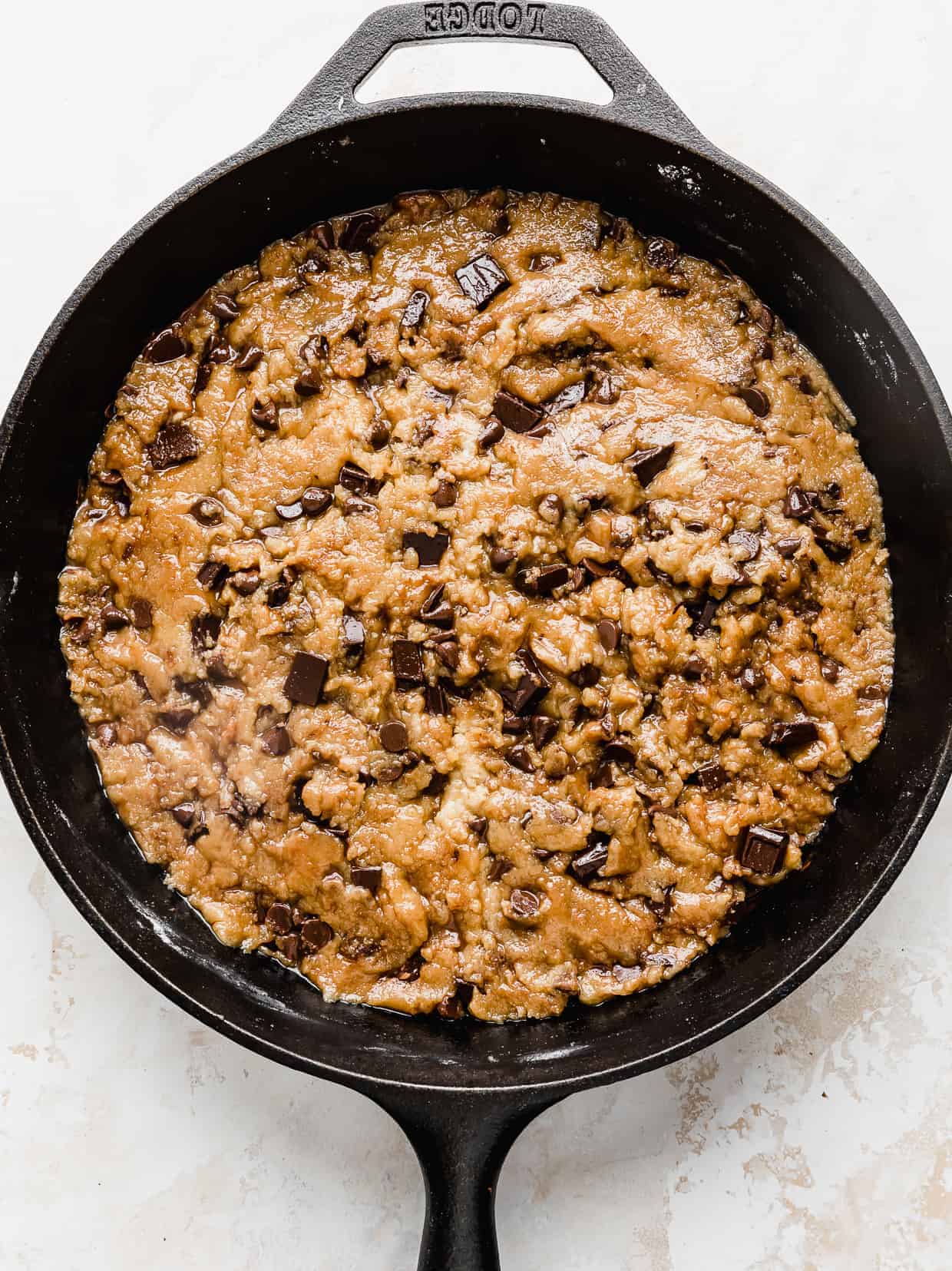 An unbaked pizookie (skillet chocolate chip cookie) in a cast iron skillet against a textured white background. 