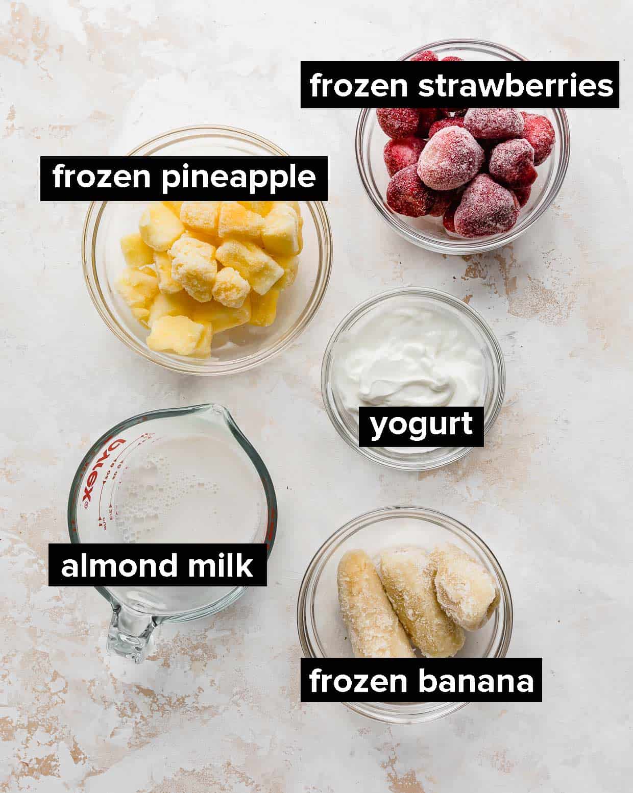 Ingredients used to make strawberry pineapple smoothie; milk, banana, strawberries, yogurt, and pineapple.