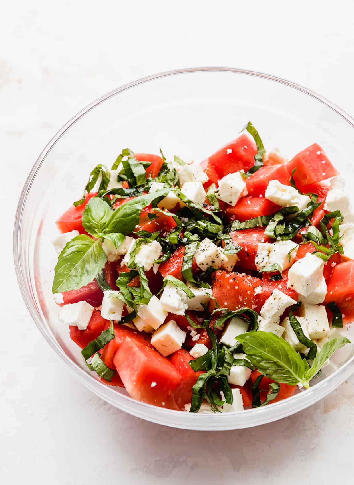 A Watermelon Feta Basil Salad in a glass bowl against a white background.