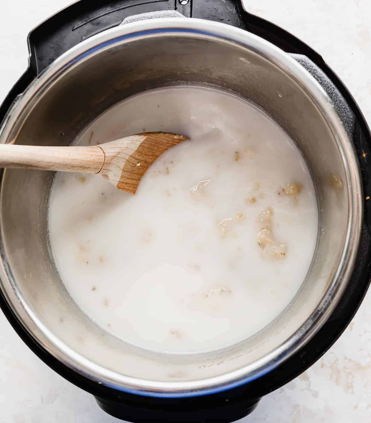 A wooden spoon stirring uncooked banana steel cut oats in an instant pot.