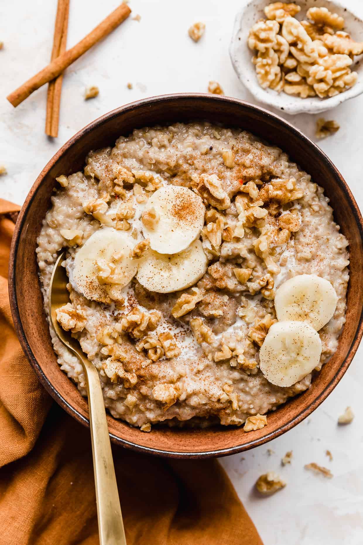 A brown bowl full of Banana Steel Cut Oats garnished with sliced bananas and nuts.