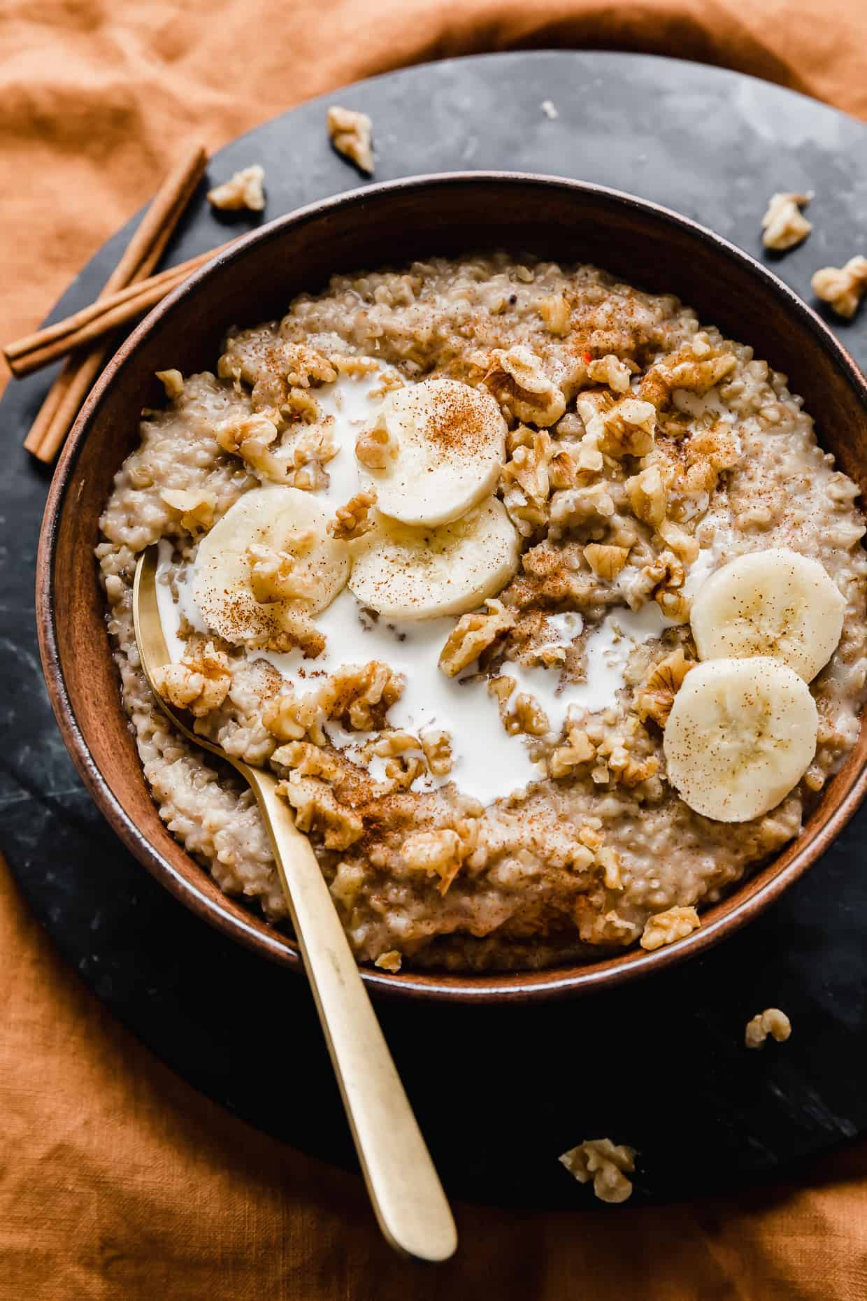 A wooden bowl full of Banana Steel Cut Oats topped with sliced bananas and walnuts against a black background.