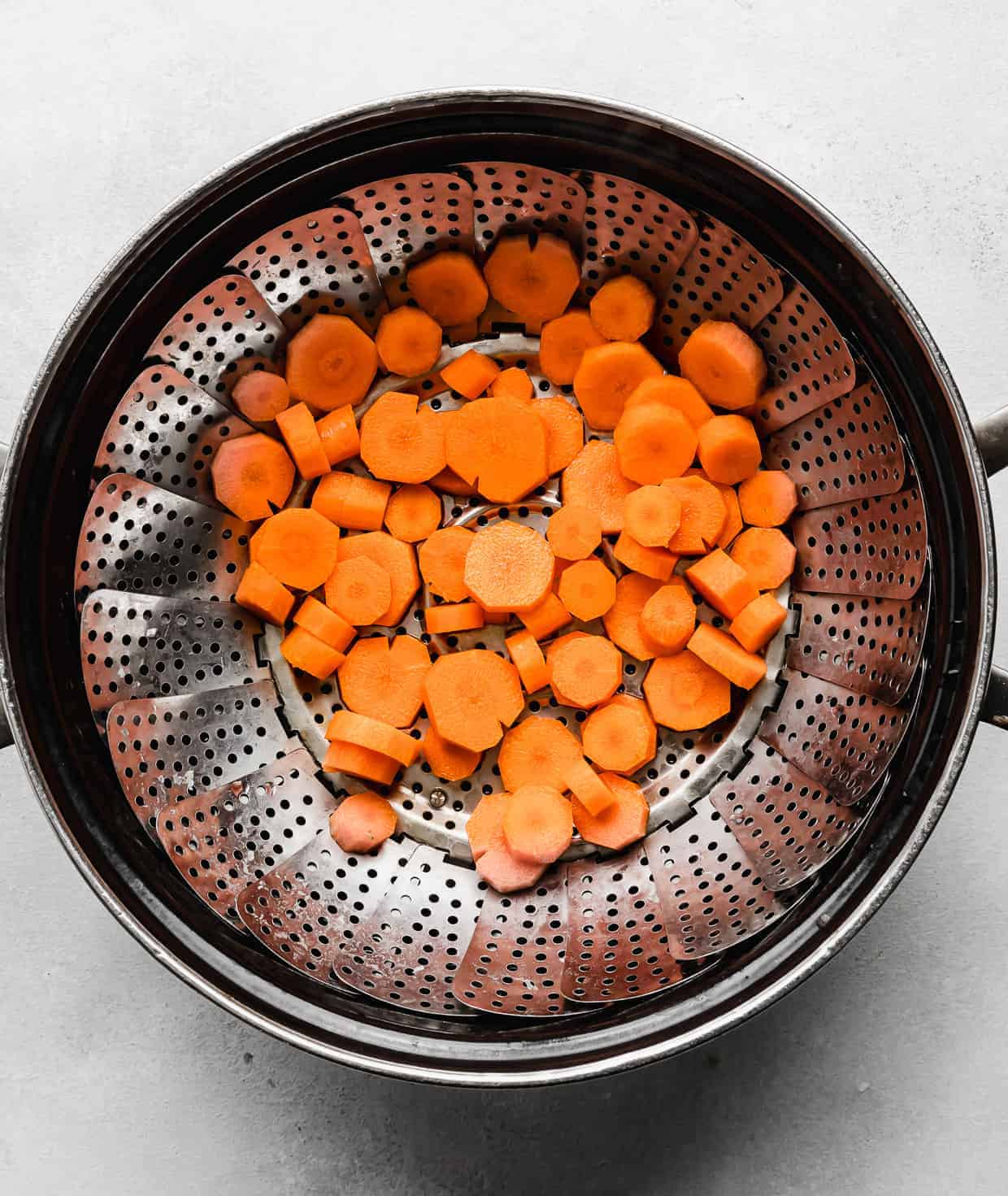 Sliced carrots in a steamer basket that's nestled in a large pot. 