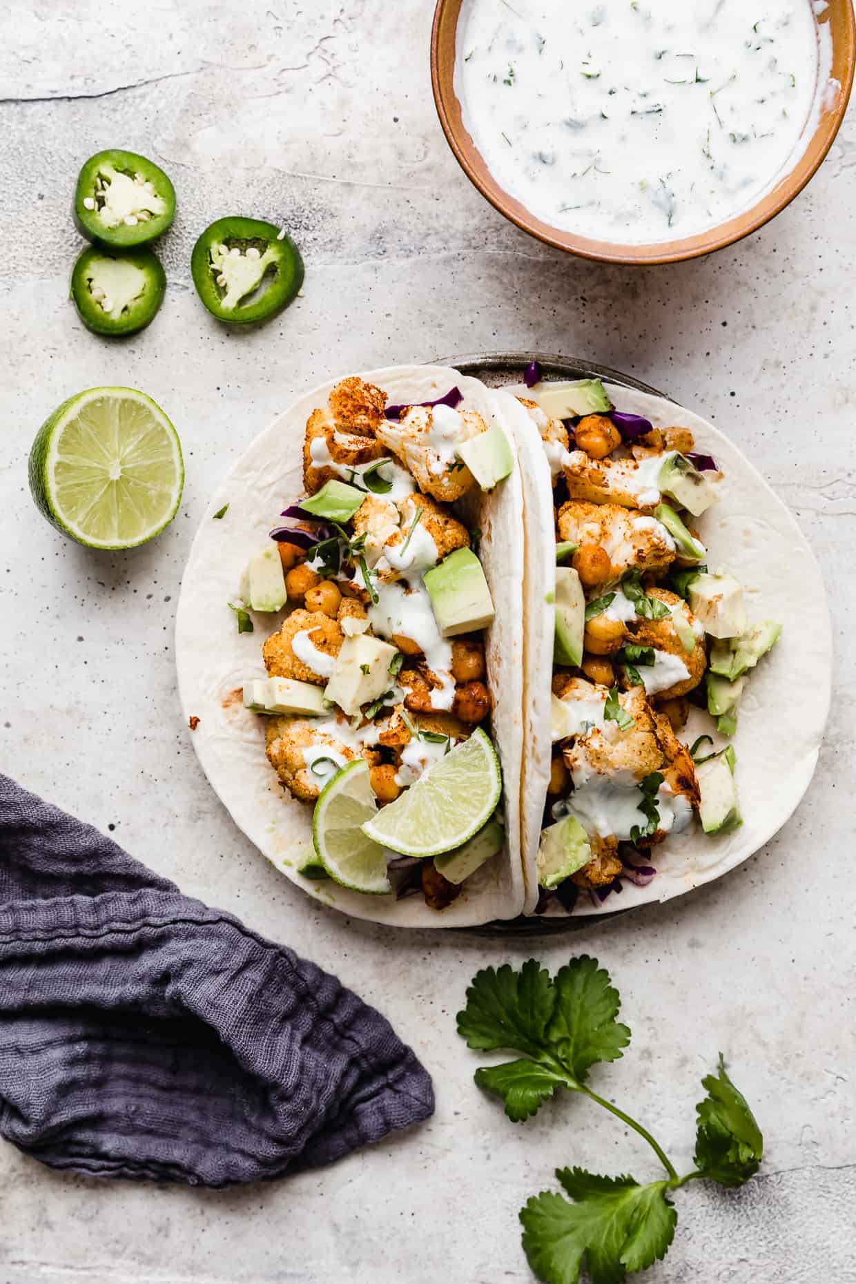 Two Roasted Cauliflower Tacos topped with a drizzle of lime crema against a white background.