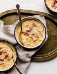 Three bowls of Ham and Corn Chowder, with one bowl on a bronze platter.