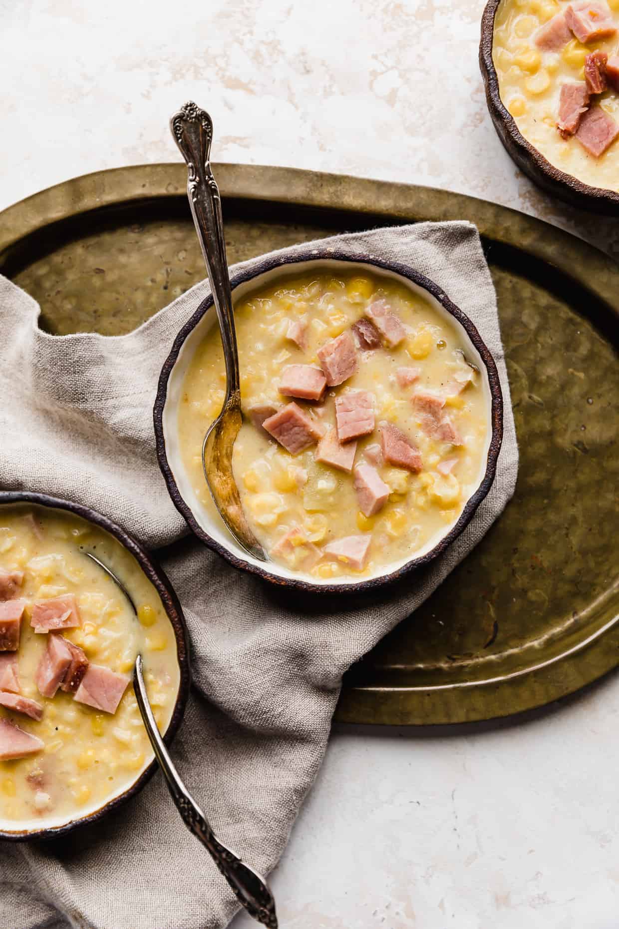 Three bowls of Ham and Corn Chowder, with one bowl on a bronze platter. 
