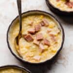 A close up of Ham and Corn Chowder in a black bowl against a white textured background.