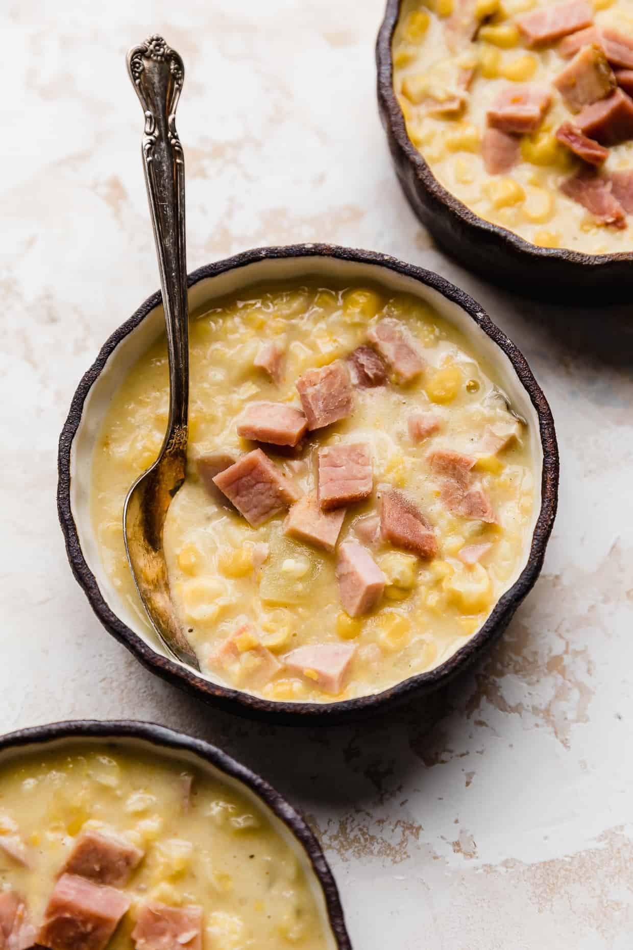 A close up of Ham and Corn Chowder in a black bowl against a white textured background.